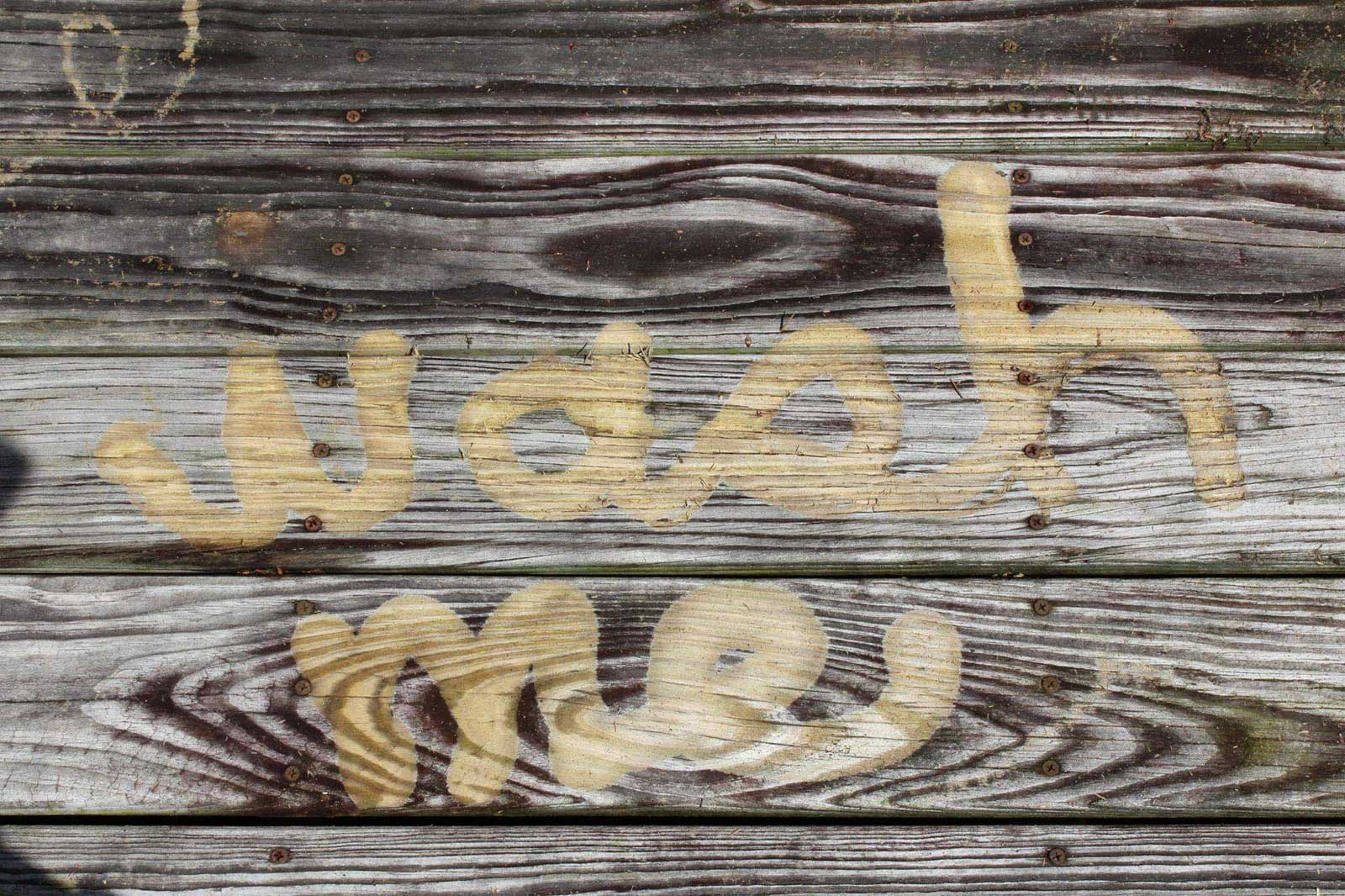 The words “wash me” pressure washed into an old, weathered deck