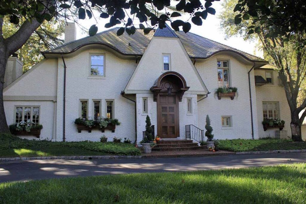 Home with steep gable and curved roofline over windows, featuring wooden front door has been repainted a timeless white