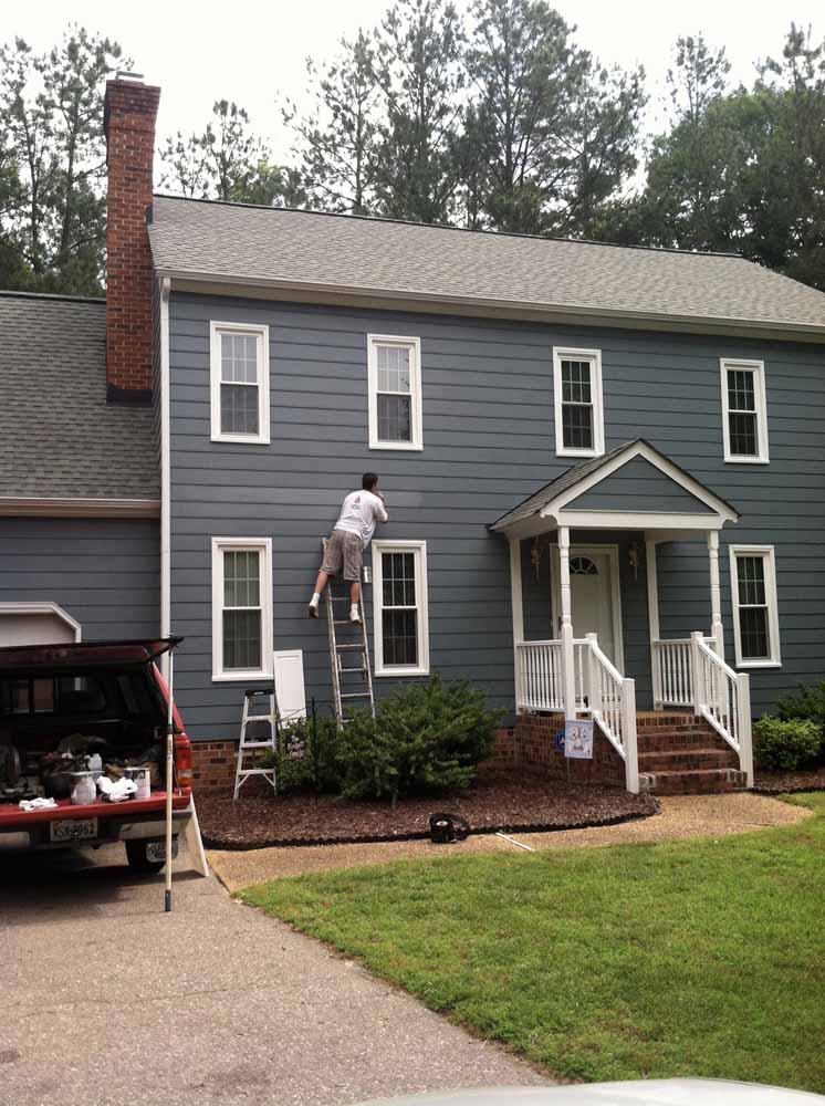 Man on a ladder repainting a slate blue house